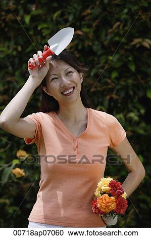 Stock Image - Woman holding trowel and bouquet of flowers, wiping her brow. Fotosearch