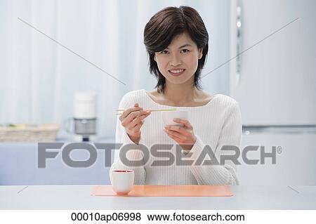 Woman in kitchen, eating with chopsticks, looking at camera View Large Photo Image Stock Photo - Woman in kitchen, eating with chopsticks, looking at camera. Fotosearch