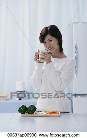 Stock Image - Woman in kitchen, holding a mug, looking at camera. Fotosearch