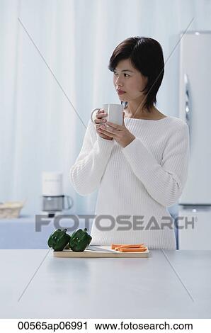 Woman in kitchen, holding mug, looking away View Large Photo Image Stock Image - Woman in kitchen, holding mug, looking away. Fotosearch