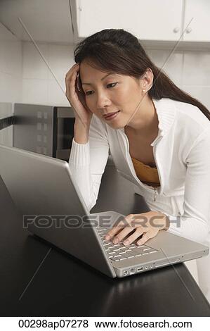 Woman in kitchen leaning on counter staring at laptop / computer, with head resting on hand View Large Photo Image Stock Photo - Woman in kitchen leaning on counter staring at laptop / computer, with head resting on hand. Fotosearch