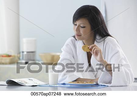 Stock Photo - woman in kitchen wearing bathrobe, holding cooking, reading magazine. Fotosearch