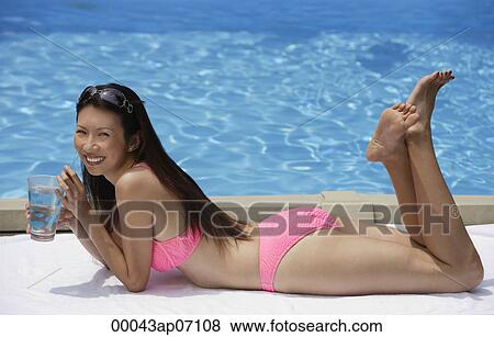 Woman in pink bikini, lying by swimming pool, holding a glass of water View Large Photo Image Stock Photo - Woman in pink bikini, lying by swimming pool, holding a glass of water. Fotosearch