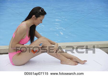 Woman in pink bikini, sitting by swimming pool, applying sun tan lotion on her legs View Large Photo Image Stock Photography - Woman in pink bikini, sitting by swimming pool, applying sun tan lotion on her legs. Fotosearch