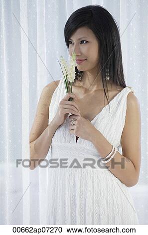 woman in white dress holding flowers and smelling flowers View Large Photo Image Stock Image - woman in white dress holding flowers and smelling flowers. Fotosearch