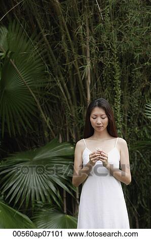 Woman in white dress, standing outdoors, looking at flower in her hand View Large Photo Image Stock Image - Woman in white dress, standing outdoors, looking at flower in her hand. Fotosearch