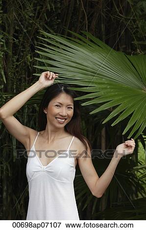 Woman in white top, standing under big leaf, smiling at camera View Large Photo Image Stock Photo - Woman in white top, standing under big leaf, smiling at camera. Fotosearch