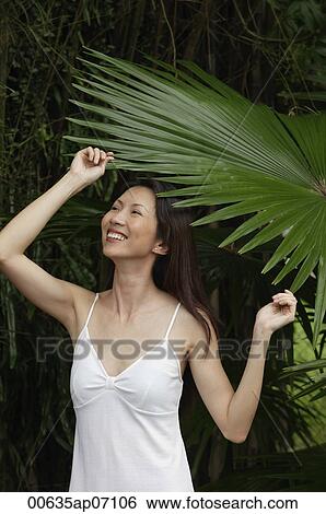 Stock Photograph - Woman in white top, standing under big leaf. Fotosearch