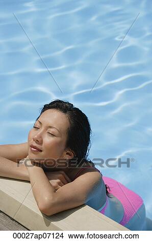 Woman leaning at the edge of swimming pool, arms crossed, eyes closed, high angle view View Large Photo Image Picture - Woman leaning at the edge of swimming pool, arms crossed, eyes closed, high angle view. Fotosearch