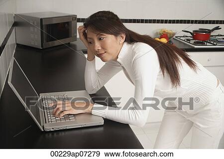 Woman leaning on counter, looking at laptop / computer. View Large Photo Image Stock Photo - Woman leaning on counter, looking at laptop / computer.. Fotosearch