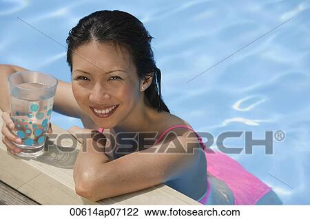 Woman leaning on edge of swimming pool, holding a drink, smiling at camera View Large Photo Image Stock Image - Woman leaning on edge of swimming pool, holding a drink, smiling at camera. Fotosearch
