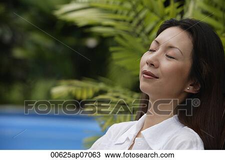 Stock Image - Woman outdoors, eyes closed, head shot. Fotosearch