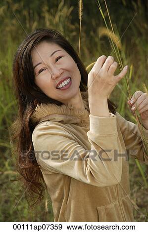 Woman outside standing in tall grass, smiling at camera View Large Photo Image Stock Photo - Woman outside standing in tall grass, smiling at camera. Fotosearch