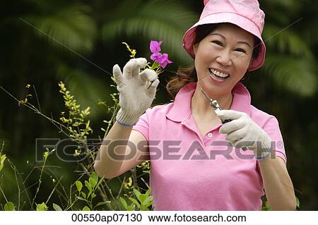 Stock Image - Woman pruning plants, smiling at camera. Fotosearch