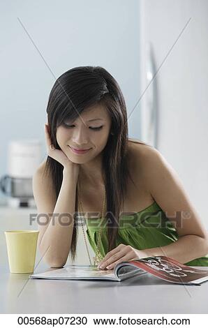 Stock Image - Woman reading magazine in kitchen. Fotosearch