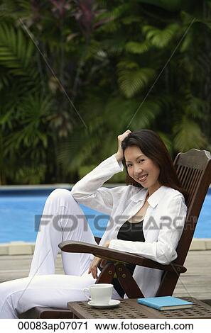 Woman sitting by swimming pool, smiling at camera, hand on head View Large Photo Image Stock Image - Woman sitting by swimming pool, smiling at camera, hand on head. Fotosearch