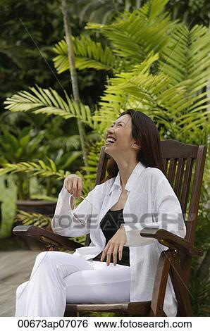 Woman sitting in garden, smiling, looking up View Large Photo Image Stock Photograph - Woman sitting in garden, smiling, looking up. Fotosearch