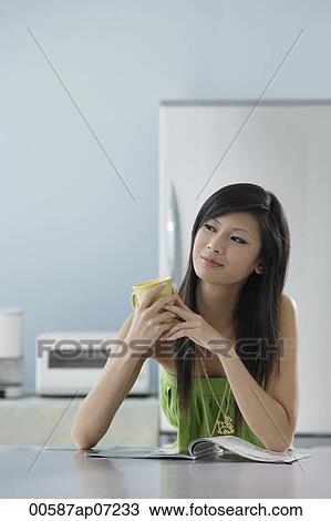 woman sitting in kitchen with magazine holding mug View Large Photo Image Stock Image - woman sitting in kitchen with magazine holding mug. Fotosearch