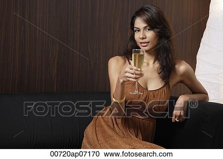 Woman sitting on couch, holding champagne glass, smiling at camera View Large Photo Image Stock Image - Woman sitting on couch, holding champagne glass, smiling at camera. Fotosearch