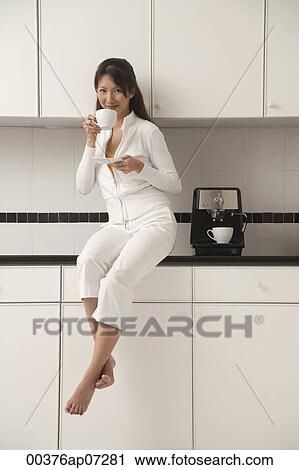 Woman sitting on counter in kitchen next to cappuccino machine, drinking coffee and looking at camera. View Large Photo Image Stock Image - Woman sitting on counter in kitchen next to cappuccino machine, drinking coffee and looking at camera.. Fotosearch