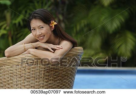 Woman sitting on rattan chair, smiling at camera, wearing flower View Large Photo Image Stock Photo - Woman sitting on rattan chair, smiling at camera, wearing flower. Fotosearch