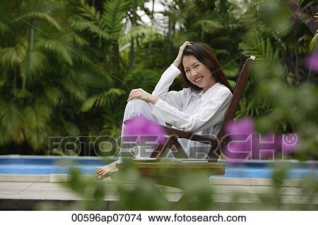 Picture - Woman sitting outdoors, hand on head, smiling at camera. Fotosearch