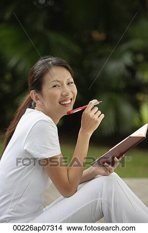 woman sitting outside in tropical setting, writing in journal, diary. looking at camera, smiling. View Large Photo Image Picture - woman sitting outside in tropical setting, writing in journal, diary. looking at camera, smiling.. Fotosearch
