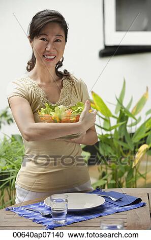 Woman standing at outdoor table, holding bowl of salad View Large Photo Image Stock Image - Woman standing at outdoor table, holding bowl of salad. Fotosearch