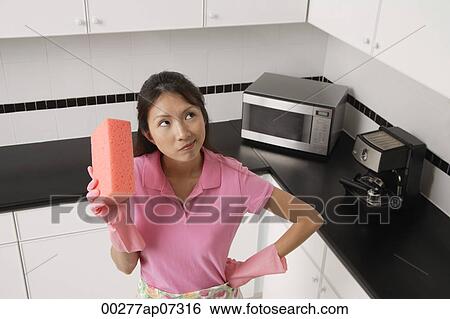 woman standing in kitchen, wearing gloves and apron for cleaning, holding sponge and thinking. View Large Photo Image Stock Photograph - woman standing in kitchen, wearing gloves and apron for cleaning, holding sponge and thinking.. Fotosearch