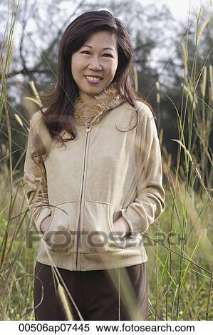 Woman standing in tall grass, hands in pocket, smiling at camera, nature View Large Photo Image Stock Photography - Woman standing in tall grass, hands in pocket, smiling at camera, nature. Fotosearch
