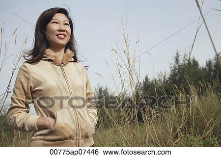 Woman standing in tall grass, nature, looking up to sky View Large Photo Image Stock Photograph - Woman standing in tall grass, nature, looking up to sky. Fotosearch