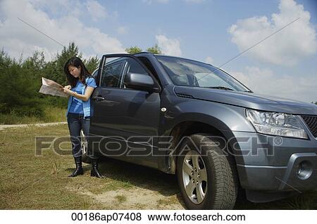 Woman standing next to SUV, looking at map View Large Photo Image Stock Photo - Woman standing next to SUV, looking at map. Fotosearch