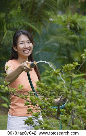 Woman watering plants in garden, smiling at camera View Large Photo Image Stock Image - Woman watering plants in garden, smiling at camera. Fotosearch