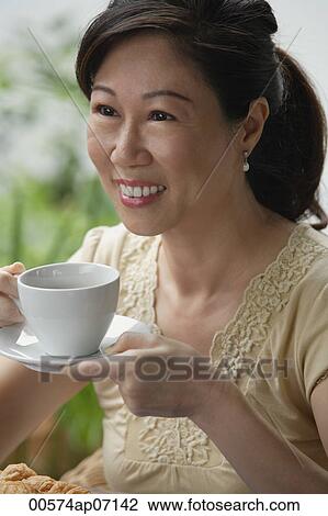 Woman with cup and saucer, having a drink, smiling View Large Photo Image Stock Image - Woman with cup and saucer, having a drink, smiling. Fotosearch