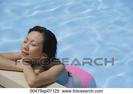 Stock Photography - Woman with eyes closed, leaning on the edge of swimming pool. Fotosearch