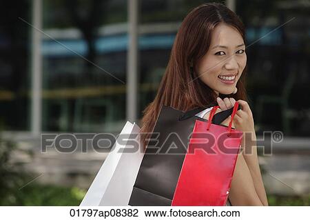 Stock Image - Woman with shopping bags, smiling over shoulder at camera. Fotosearch