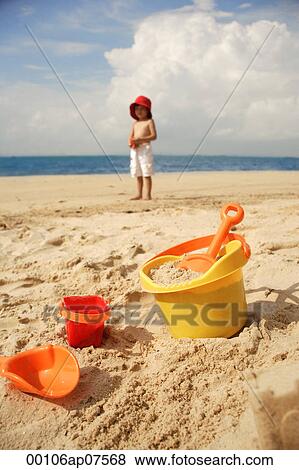 Young boy on beach, beach bucket and toys in foreground View Large Photo Image Stock Photo - Young boy on beach, beach bucket and toys in foreground. Fotosearch