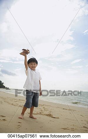 Stock Image - young boy on beach flying wooden airplane. Fotosearch