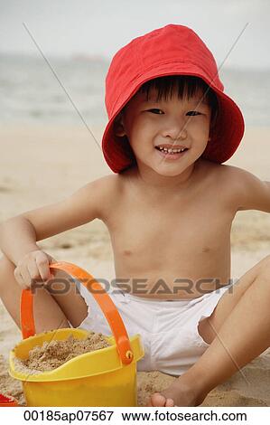 Young boy sitting on beach, wearing read hat and holding yellow beach bucket View Large Photo Image Stock Photo - Young boy sitting on beach, wearing read hat and holding yellow beach bucket. Fotosearch