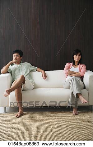 Young couple sitting on opposite ends of the sofa View Large Photo Image Stock Photo - Young couple sitting on opposite ends of the sofa. Fotosearch