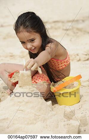 Stock Photo - Young girl building sand castle on beach. Fotosearch