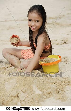 Young girl building sand castle on beach, smiling View Large Photo Image Stock Photo - Young girl building sand castle on beach, smiling. Fotosearch