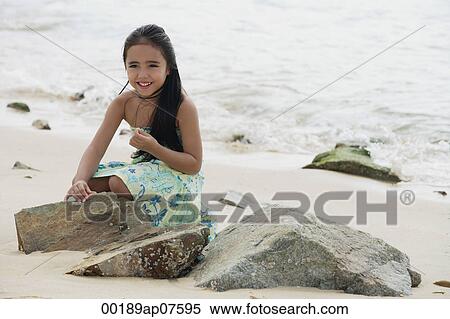Young girl sitting on beach by rocks View Large Photo Image Stock Photography - Young girl sitting on beach by rocks. Fotosearch