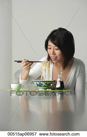 Stock Photo - Young woman eating a bowl of noodles. Fotosearch