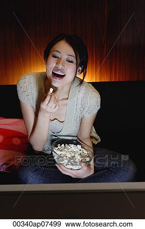 Young woman eating popcorn and watching TV, smiling View Large Photo Image Stock Photo - Young woman eating popcorn and watching TV, smiling. Fotosearch