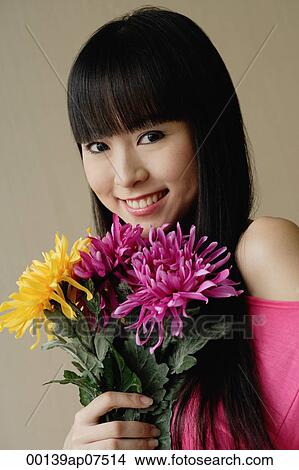 Young woman holding bouquet of flowers, smiling at camera View Large Photo Image Picture - Young woman holding bouquet of flowers, smiling at camera. Fotosearch