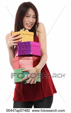 Stock Image - Young woman holding four presents, smiling at camera. Fotosearch