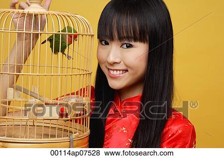Stock Photo - Young woman holding lovebird in bird cage, smiling. Fotosearch