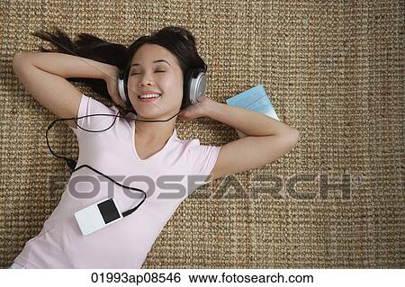 Young woman listening to music while lying down View Large Photo Image Stock Photograph - Young woman listening to music while lying down. Fotosearch