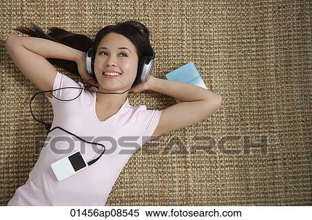 Young woman listening to music while lying down View Large Photo Image Stock Photography - Young woman listening to music while lying down. Fotosearch